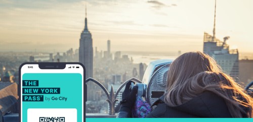 Turista osserva lo skyline di New York e l'Empire attraverso un binocolo al tramonto dal Top of The Rock, con sovrapposto uno smartphone che mostra l'app The New York Pass by Go City
