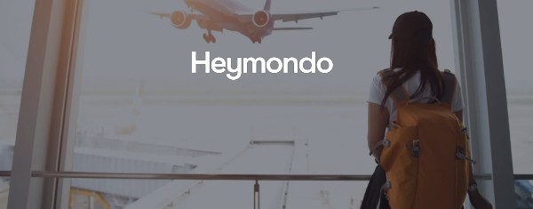 Logo Heymondo sovrapposto all'immagine di una ragazza in aeroporto che osserva dalle vetrate un aereo in fase di decollo