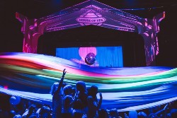 Pista da ballo gremita di gente, luci soffuse e giochi psichedelici. Una decorazione luminosa sullo sfondo incornicia il palcoscenico ed evidenzia il logo del locale House of Yes